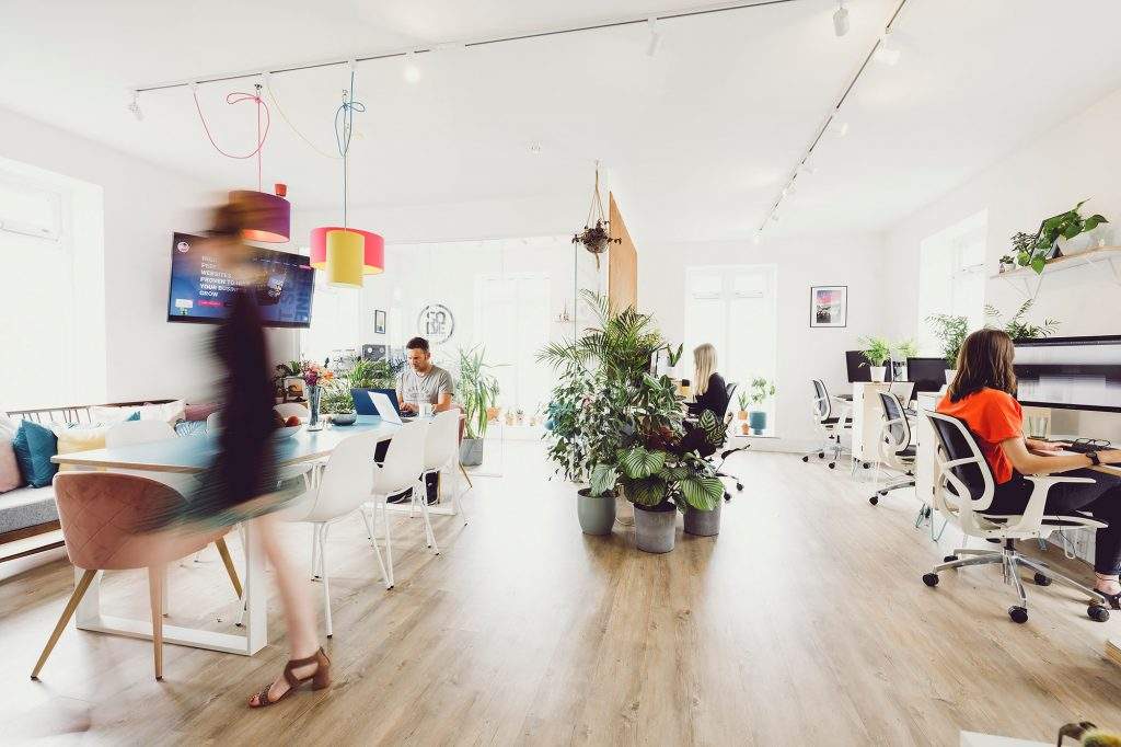 Solve office letting in lots of natural light with people busy at work at their desks and girl walking in forefront