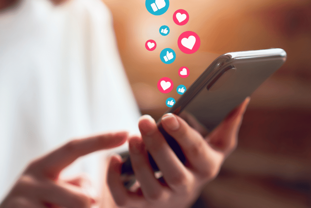 Current Social Media Trends: Four Shifts Businesses Can't Ignore in 2026 5 A mobile phone in hand, with social media heart and thumbs up icons coming out of screen