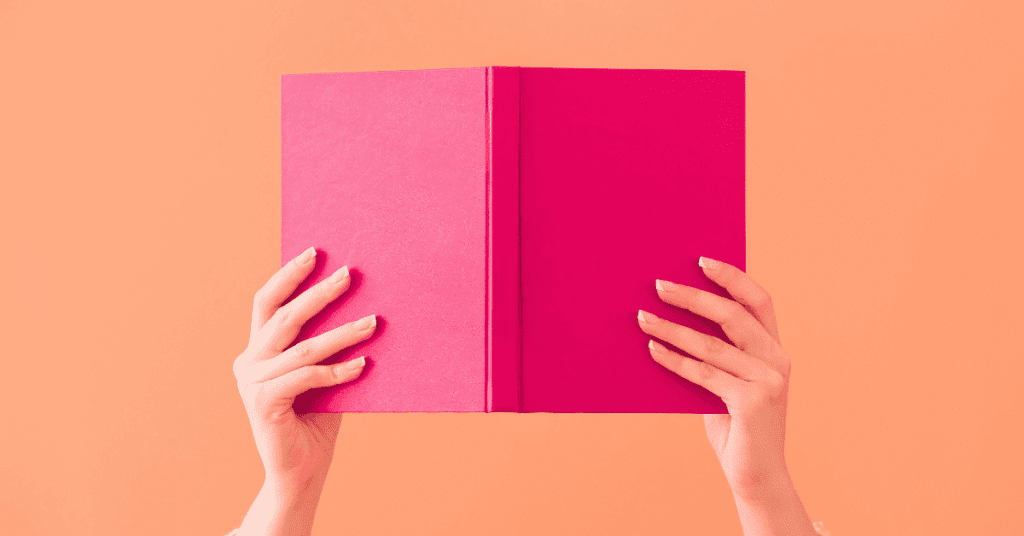 Hands holding up a pink book on an orange background to give contect to storytelling in content creation