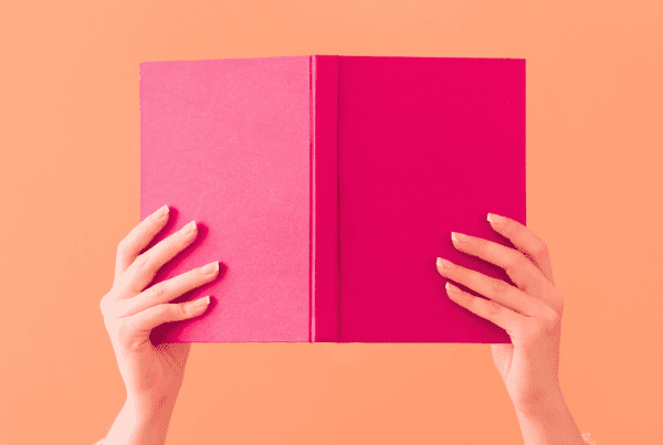 Hands holding up a pink book on an orange background to give contect to storytelling in content creation