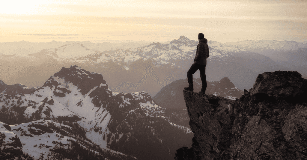 A man standing on the edge of a rock face looking out at mountains in front of him to symbolise digital marketing thought leadership