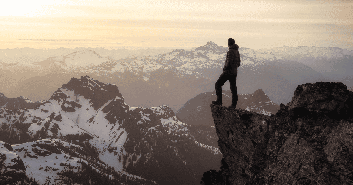 A man standing on the edge of a rock face looking out at mountains in front of him to symbolise digital marketing thought leadership