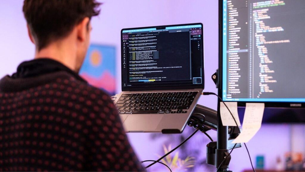 How Custom Website Development Drives Business Growth 2 Man at a stand up desk working on custom website design for a client, with coding on his laptop