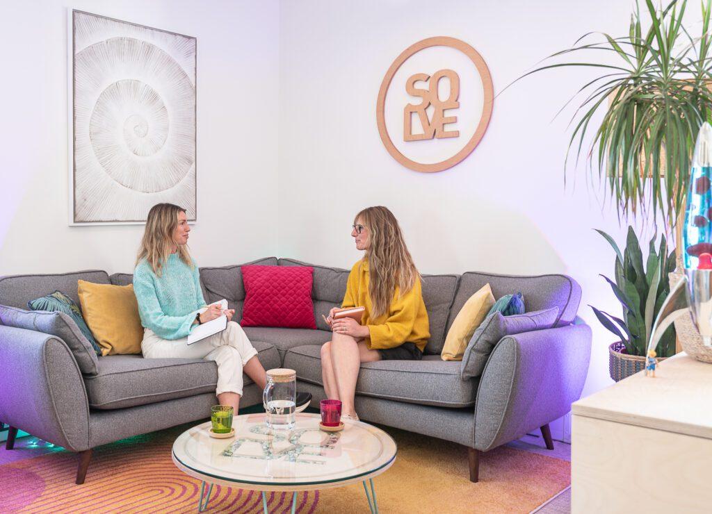 SEO Content Creation That Connects Users and Search Engines 5 Two women sat on a sofa with notebooks discussing seo content writing in a colourful office.