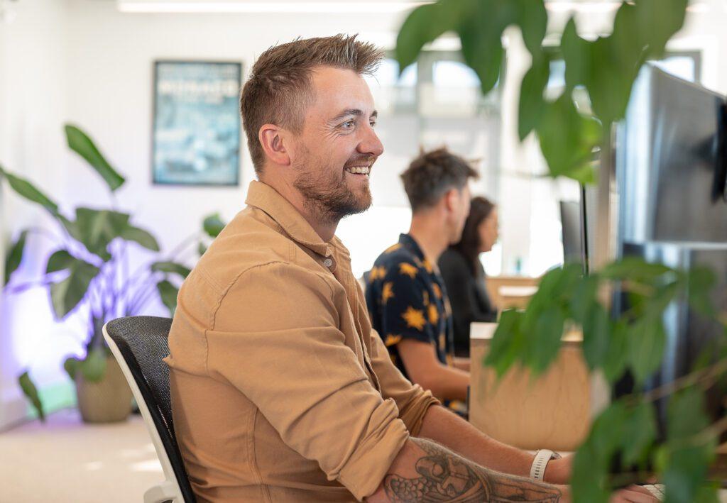 A male team member from Solve smiling and working and his desk with plants around him