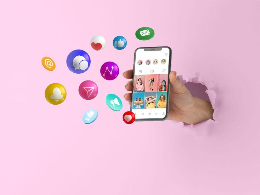 Social Media Content Planning: Expert Guide to Elevate Your Business 3 A phone showing a social media page being held against a pink background with social media symbols around it
