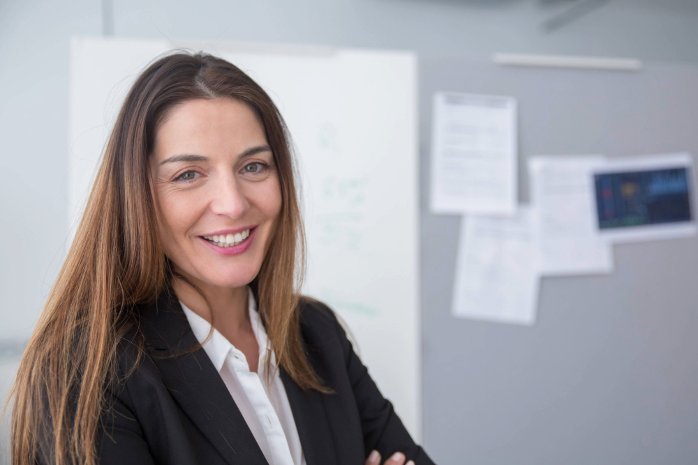 Brunette haired lady, in an office jacket, smiling.