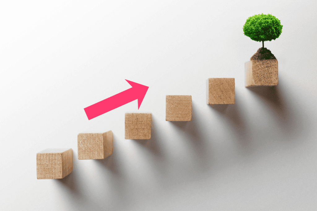 wooden stepping ladder with small tree on top, a pink arrow pointing upwards toward the tree