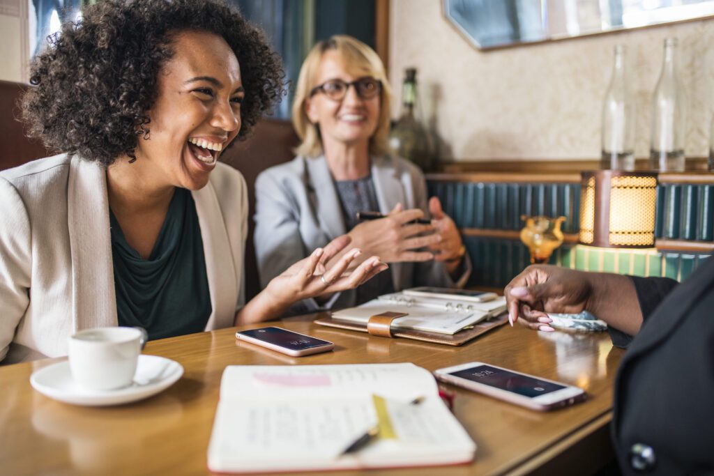 women laughing at a table in a cafe with pens and planners out on the table.