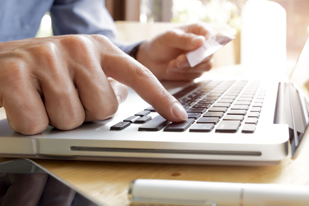 A close up image of a man holding a debit card pressing enter on his keyboard.