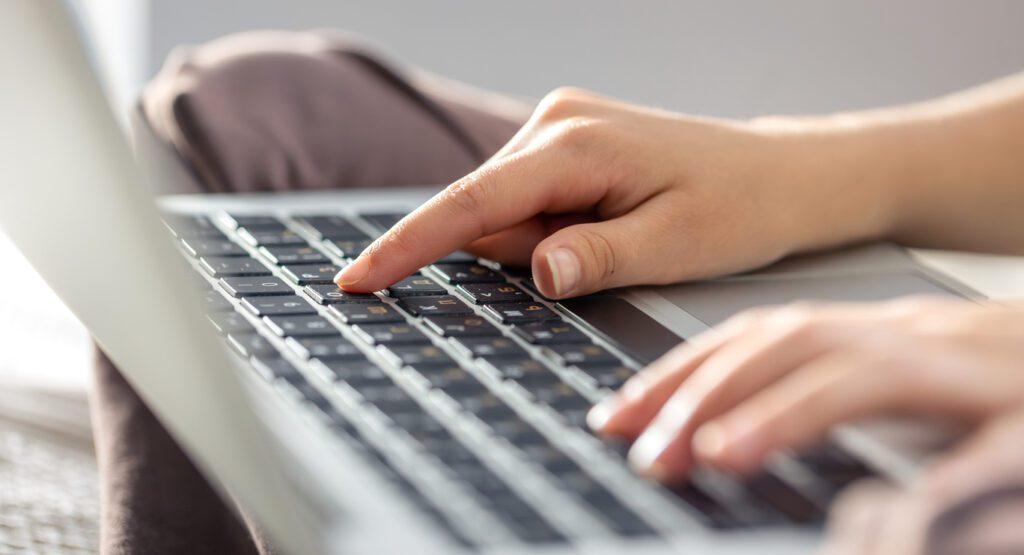 A close up of a woman typing on her laptop in a bright light room.