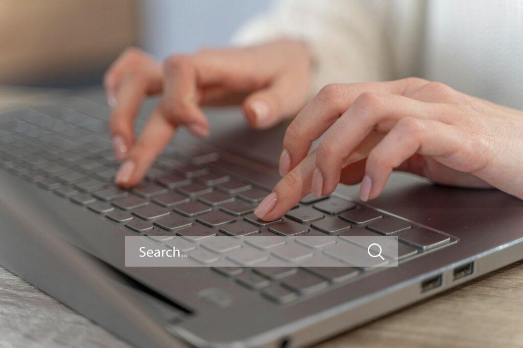 11 Common PPC Mistakes to Avoid in Your Next Campaign 2 A lady types on a laptop keyboard with a graphic of a search bar over the image.