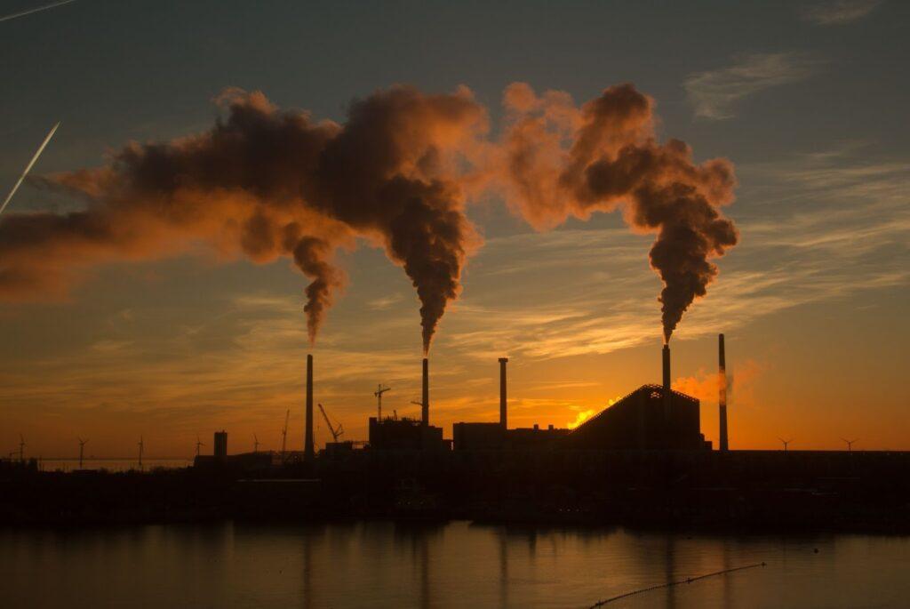 A sunset image of a fossil fuel site with smoke coming out of the chimneys.