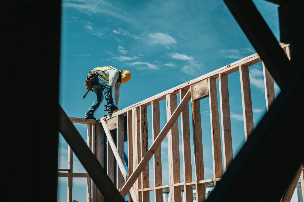 A construction man, in a hard hat, drilling into a wooden building frame.