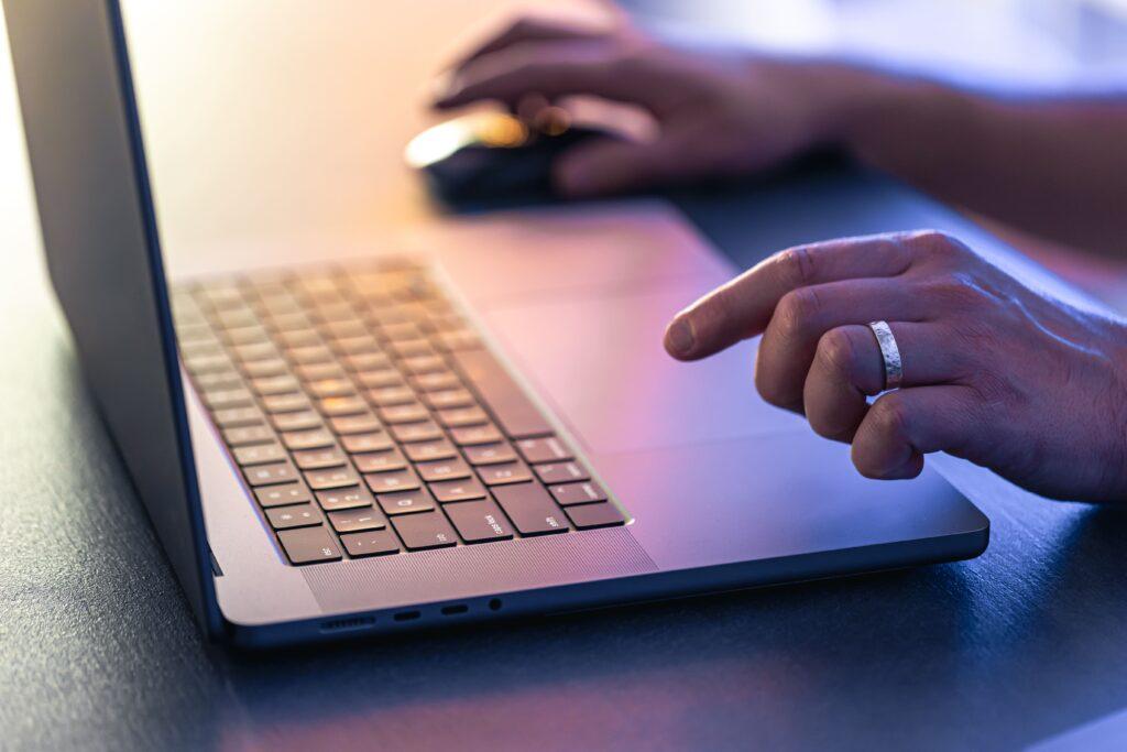 11 Common PPC Mistakes to Avoid in Your Next Campaign 2 common ppc mistakes represented through a laptop in purple light on a table, with a hand on a mouse about to click.