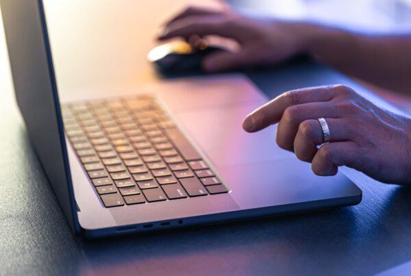 11 Common PPC Mistakes to Avoid in Your Next Campaign 28 common ppc mistakes represented through a laptop in purple light on a table, with a hand on a mouse about to click.