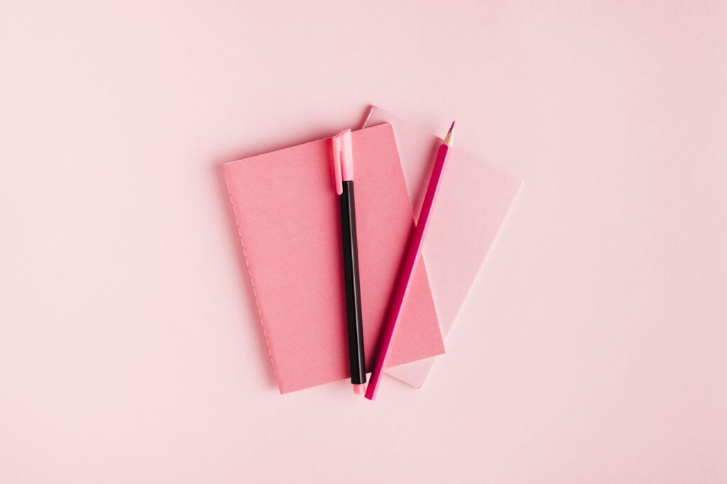 Pink paper background with two pink planners laying on one another, with a pink pen and pencil on top representing content planning tips.