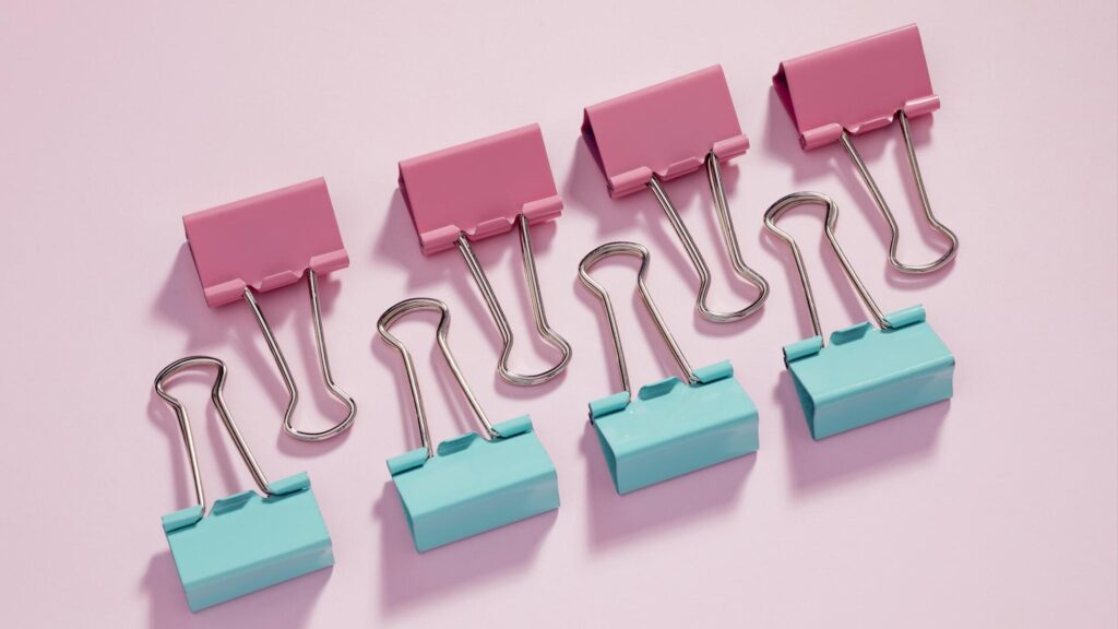 Why Your Social Media Brand Voice Matters More Than You Think 3 A line of paper alternating pink and blue paperclips on a pink background.