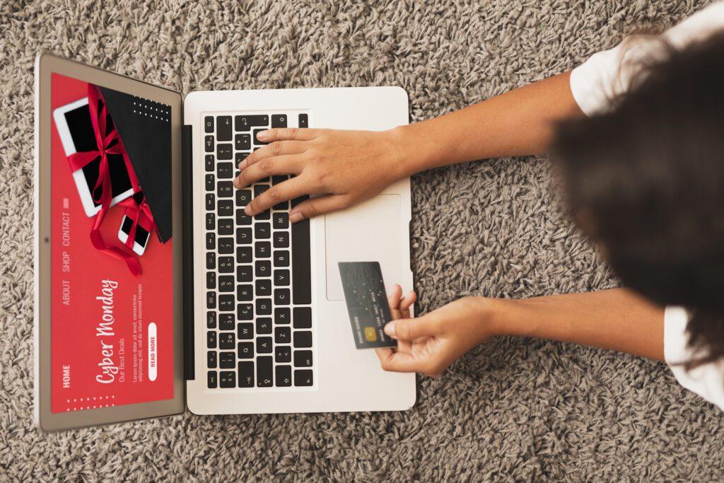 An ariel view of a woman lying on the carpet with her credit card and laptop infront of her, getting ready to purchase something from a website with good user experience and user interface.
