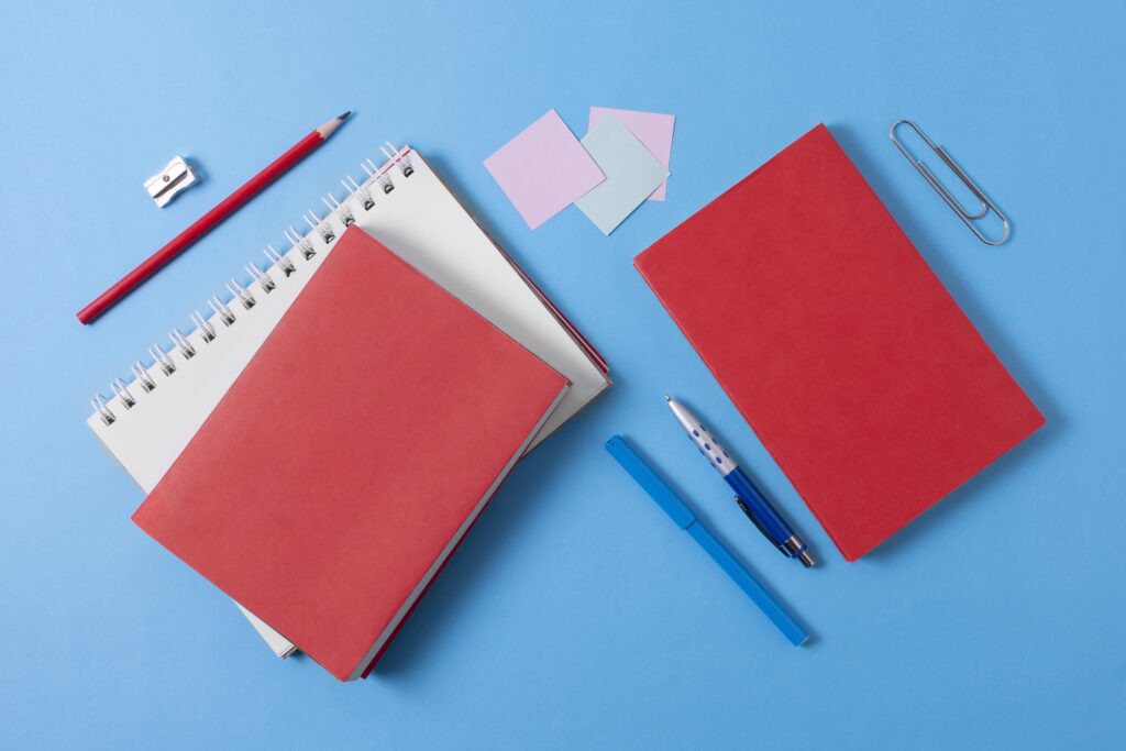 Blue background with birdseye view on red planners, blue pens and sticky notes laid out on the table.